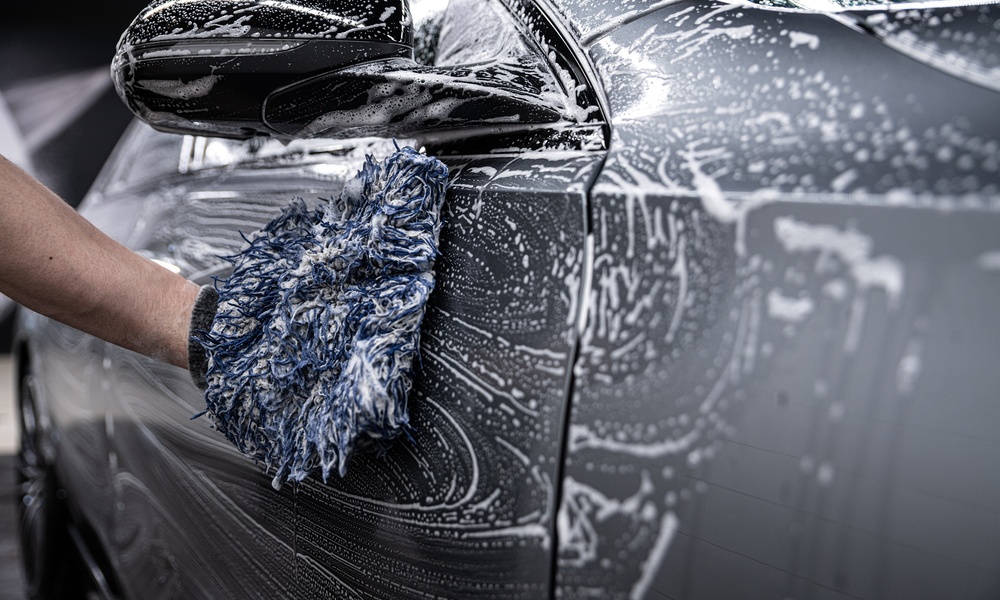 A gloved hand applying coating to a glossy black car panel near a mirror with a small applicator pad.