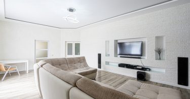 A bright living room with a sectional sofa facing a wall-mounted TV set into a white brick accent wall.