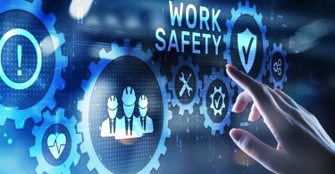 A hand touches a digital work safety interface with gears, a checklist, and shield icons on the screen.