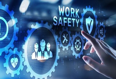 A hand touches a digital work safety interface with gears, a checklist, and shield icons on the screen.