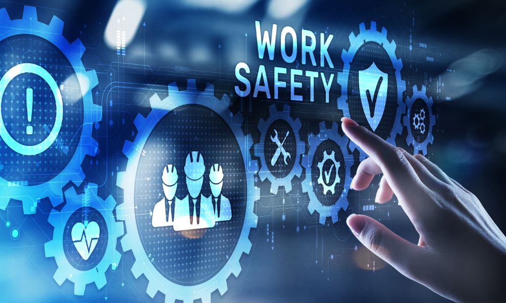 A hand touches a digital work safety interface with gears, a checklist, and shield icons on the screen.