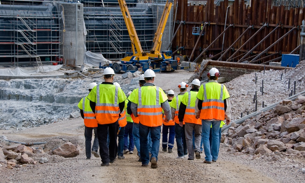 Construction workers in high-visibility vests and hard hats walking together through a large active jobsite.
