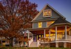 An older, residential property with a round porch on the front corner. The tree outside has brown, fallen leaves.