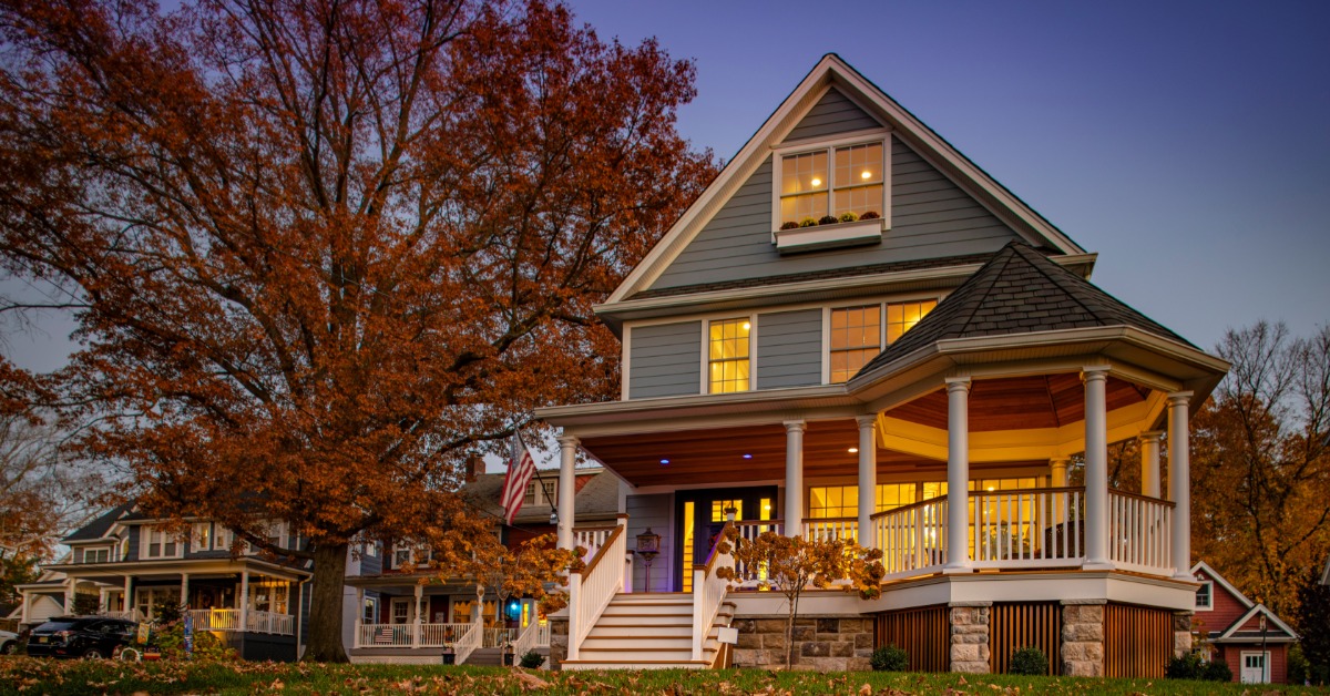 An older, residential property with a round porch on the front corner. The tree outside has brown, fallen leaves.