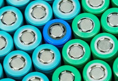 Rows of blue, turquoise, and green cylindrical battery cells arranged closely together, each with a silver metal top.