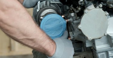 A person wearing gloves positions a silver turbocharger into a car engine, with hoses and metal parts nearby.