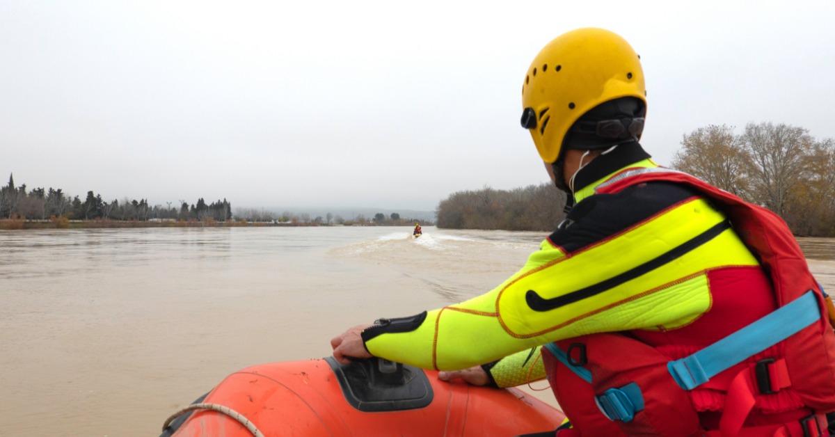 A person wearing a brightly colored wetsuit, a yellow helmet, and a red life jacket is riding in a red rescue boat.