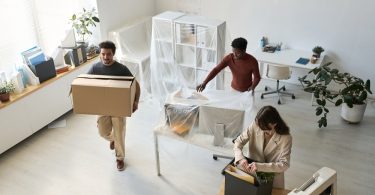 Three people are packing things up in an office environment. There is a window to the left of frame.