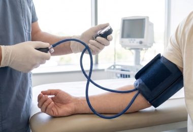 A healthcare professional wearing white latex gloves is taking the blood pressure of a male patient.