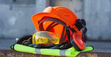 A pile of professional safety gear including a helmet, hi-vis vest, ear muffs, and thick work gloves.