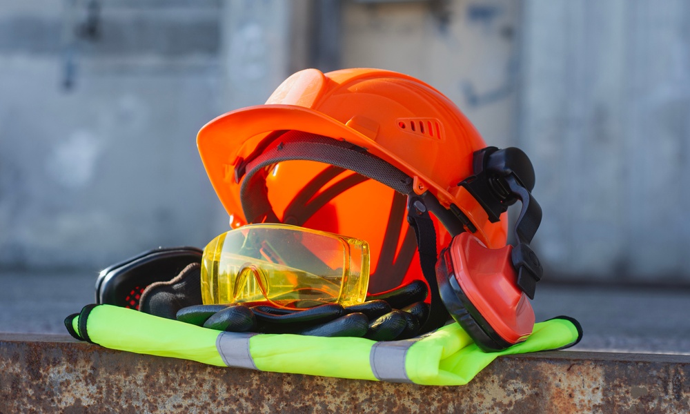 A pile of professional safety gear including a helmet, hi-vis vest, ear muffs, and thick work gloves.