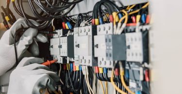 A person is working on an electrical system. They are wearing protective gloves and using a tool.