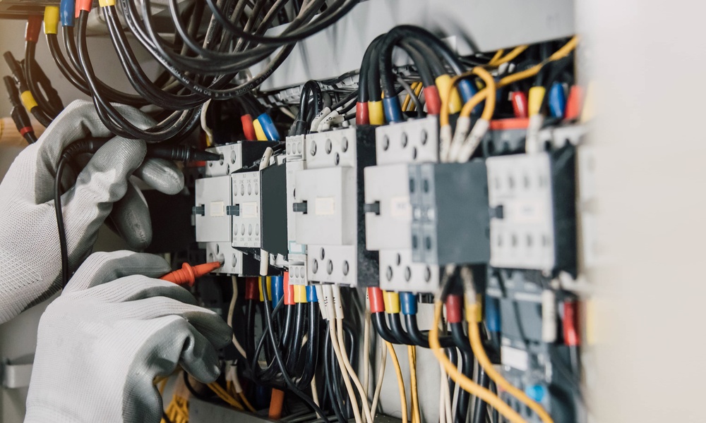 A person is working on an electrical system. They are wearing protective gloves and using a tool.