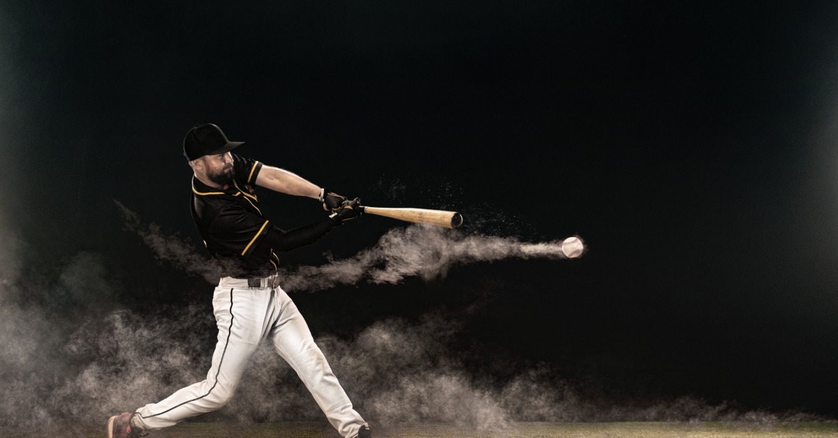 A side view of a baseball player in a black jersey with white pants swinging and contacting a baseball.