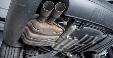 The underside of a car is visible. There is a muffler under the car that has very slight rust damage to it.