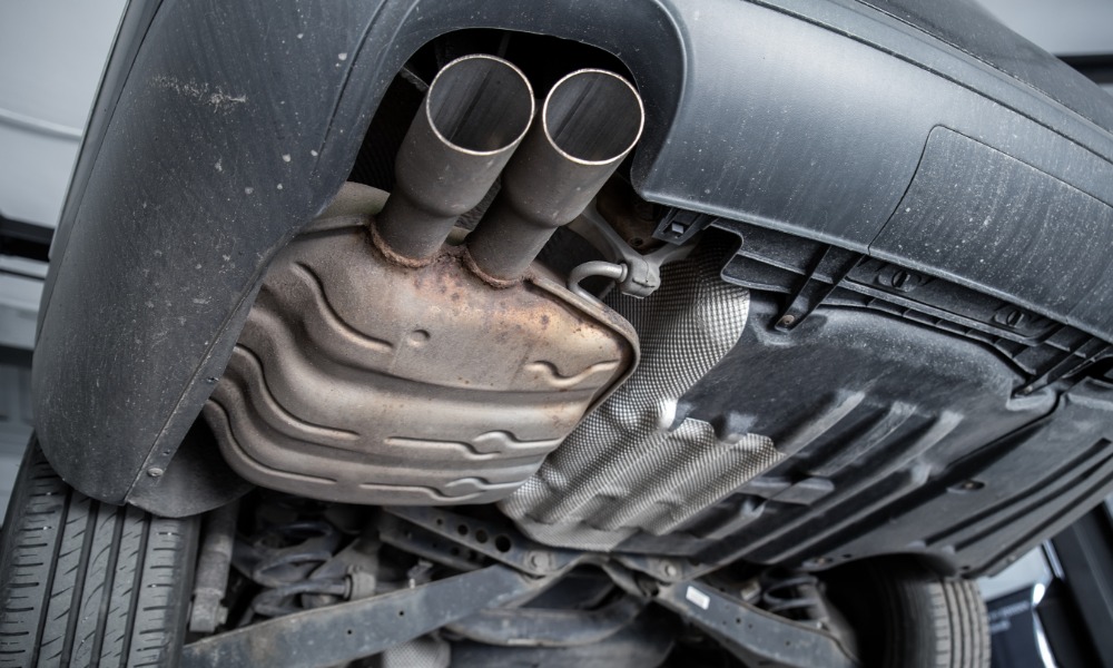The underside of a car is visible. There is a muffler under the car that has very slight rust damage to it.