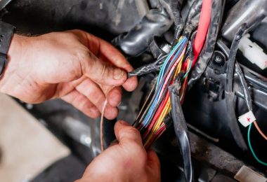 A mechanic wearing a black wristwatch moving cables attached to a car’s wiring harness in a bright room.