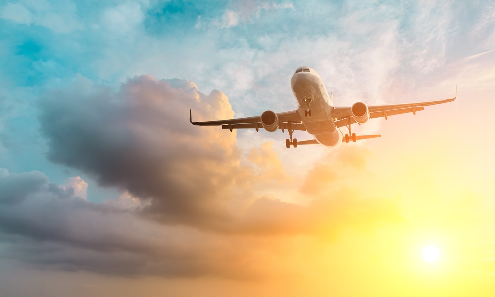 A commercial passenger airplane flying overhead with its landing gear extended against dark clouds and a golden sunset sky.