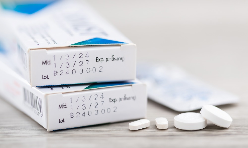 A few white medication tablets sit on the table next to the pharmacy boxes. The box shows the dates for expiry and use.