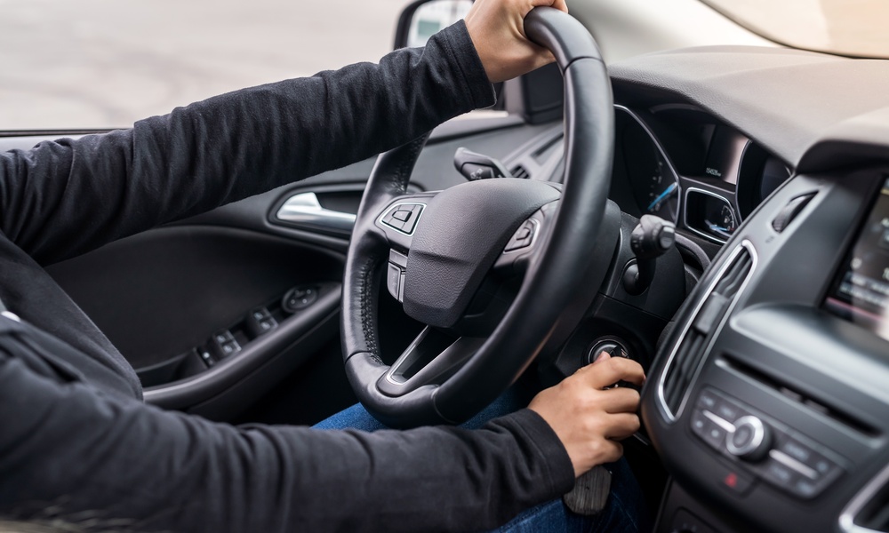 A person in a long-sleeved shirt holding a steering wheel with one hand and turning the ignition key with the other.