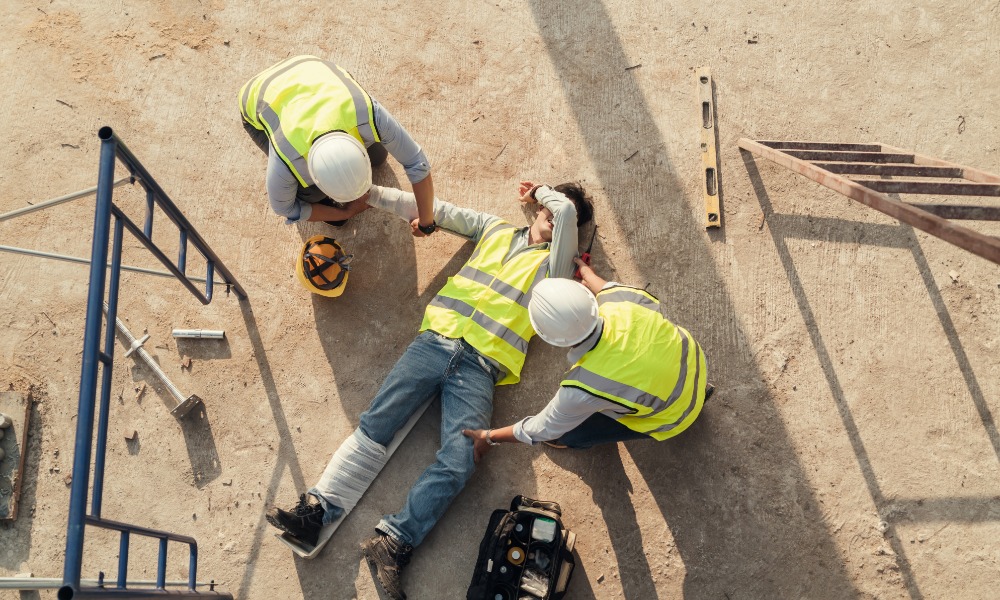 A construction worker on the ground with his leg in a cast. Two other construction workers are tending to his injuries.