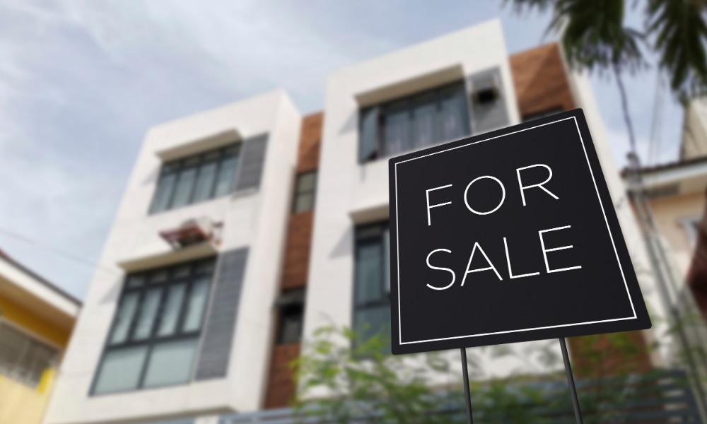 A "For Sale" sign is displayed in front of a multi-story residential building with brick accents and large windows.