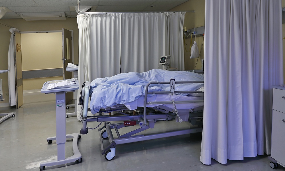 A hospital room with a moving bed covered with light blue sheets, surrounded by fabric curtains under bright light.