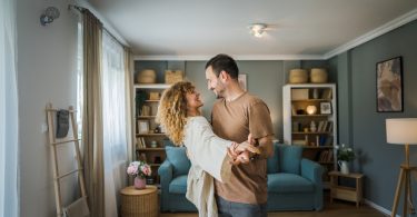 A man and a woman are standing in the middle of a living room, dancing with each other, in a residential home.