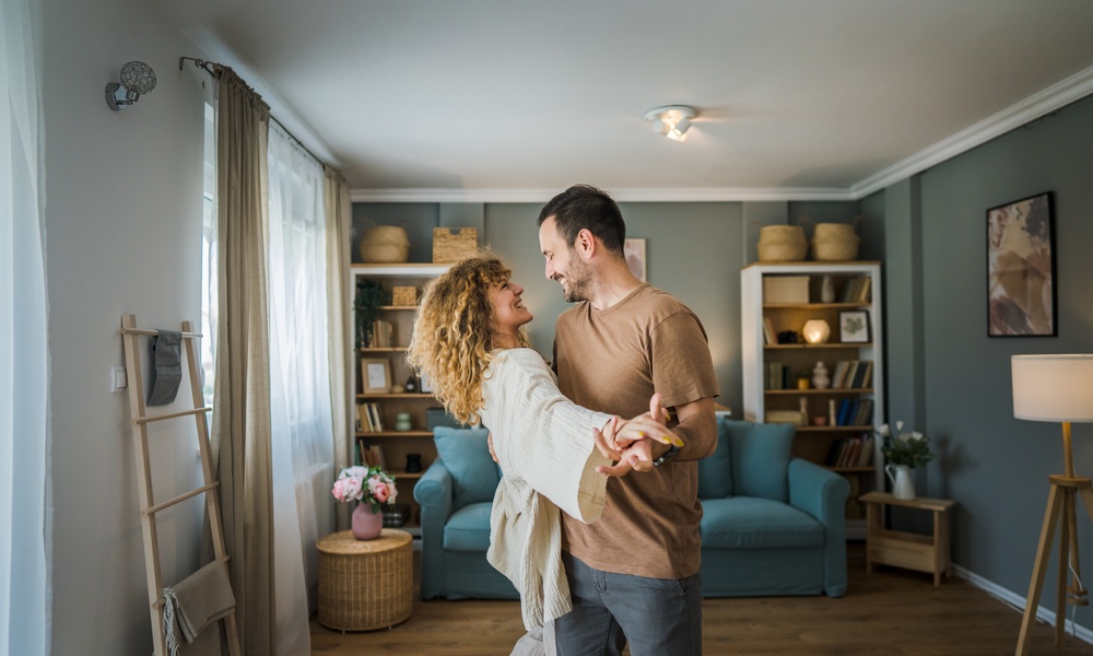 A man and a woman are standing in the middle of a living room, dancing with each other, in a residential home.