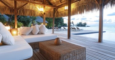 Luxury beachfront cabana with white cushioned sofas, wicker furniture, and a thatched roof overlooking an infinity pool.