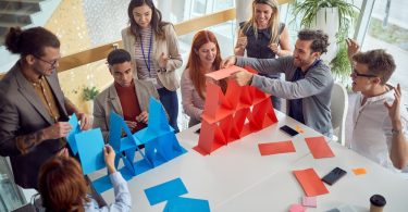 Employees construct blue and red paper structures around a conference table.