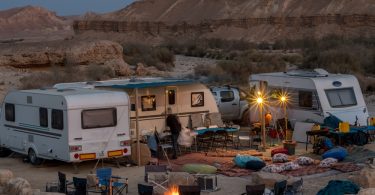 Several RVs are parked in the middle of a desert area. There is a hill in the background and it is nighttime.