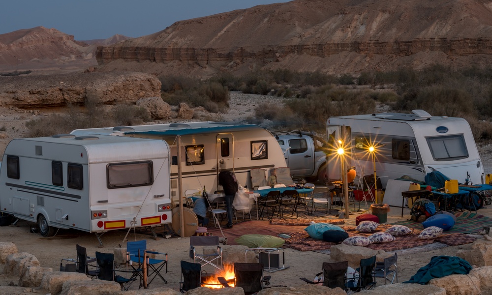 Several RVs are parked in the middle of a desert area. There is a hill in the background and it is nighttime.
