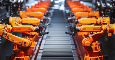 A view looking down the assembly line of a modern factory with the line flanked by numerous stationary robotic arms.