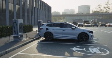 A silver SUV connects to an EV charging station in a marked parking space outside a modern office building.