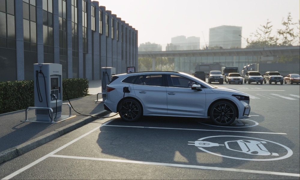 A silver SUV connects to an EV charging station in a marked parking space outside a modern office building.