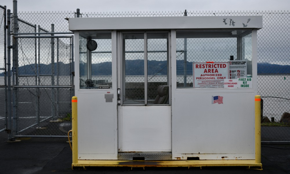 A small white security booth outside near a large lake. A red sign in the booth window reads “Restricted Area”.